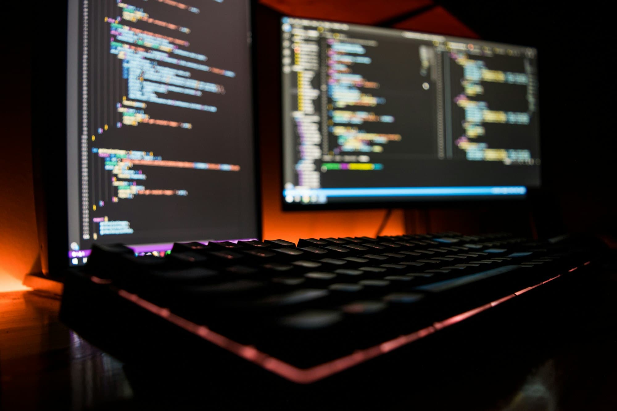 Två skärmar med programkod och ett tangentbord i mörker